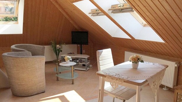 A cozy attic room with a sloped ceiling, a round glass table, a sofa, and a TV. - Apartment - Rügen-Fewo 291 (Sassnitz)