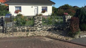 A single-story house with a sloped roof, a stone wall in front, and a metal gate. - Apartment - Rügen-Fewo 291 (Sassnitz)