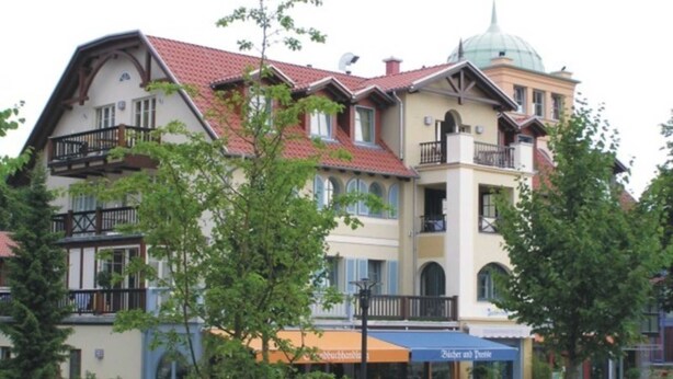 A multi-story building with balconies, a dome-shaped structure on the roof, and a storefront with an awning. - (293) 3-room apartment beach road - Apartment block LAGUNA (Kühlungsborn)