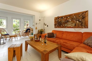 A living room with a wooden coffee table, orange sofa, wicker chairs, and a wall-mounted deer artwork.