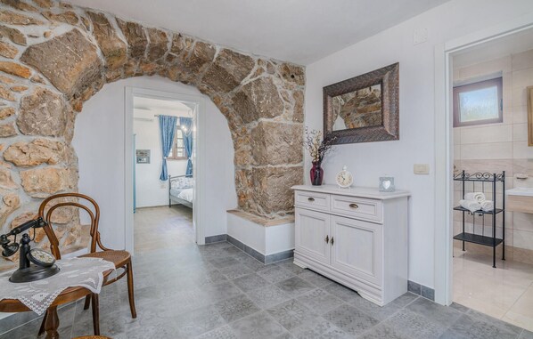 A hallway with a stone archway, a white dresser, a mirror, and a metal shelf with towels.