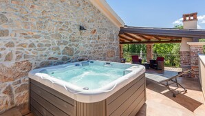 Een stenen muur, een hottub, tuinmeubilair en een pergola.