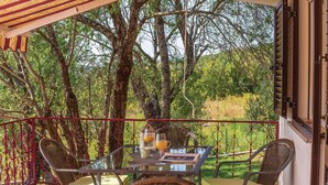 Een overdekt terras met rieten stoelen en een glazen tafel, omringd door bomen en uitzicht op het landschap.