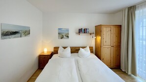 Quarto com cama, mesa de cabeceira, guarda-roupa de madeira e obras de arte na parede.