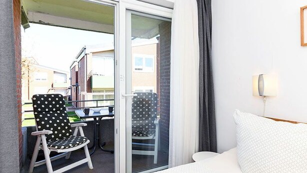 A hotel room with a bed, a chair, a table, and a view through a glass door. - Vacation apartment Treasure Island (Esens)