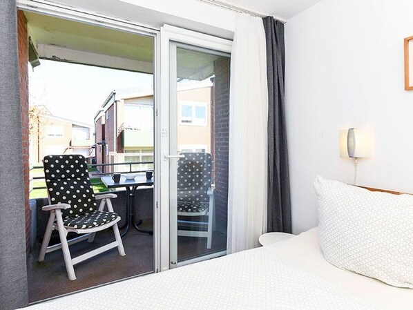 A hotel room with a bed, a chair, a table, and a view through a glass door.