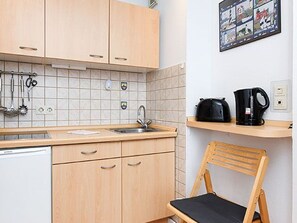 A kitchen with wooden cabinets, a sink, a coffee maker, and a chair.