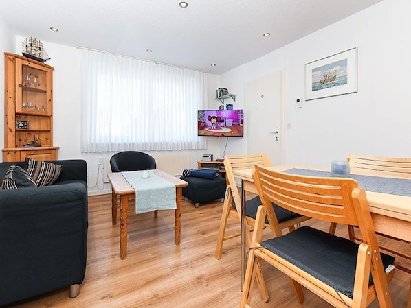 A living room with a sofa, a dining table with chairs, a television, and a window with curtains.