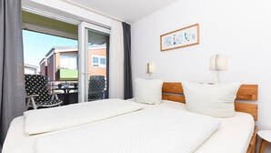 A hotel room with a large bed, two bedside tables, a chair, and a view of the outside. - Vacation apartment Treasure Island (Esens)