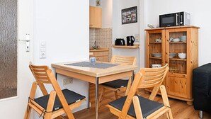 A compact kitchen with a dining table, chairs, a microwave, and a cabinet with dishes. - Vacation apartment Treasure Island (Esens)