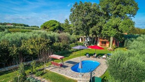 Un jardin avec une piscine, du mobilier d’extérieur et un parasol rouge.
