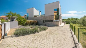 Ein modernes Haus mit gepflasterter Auffahrt, einem Garten mit Lavendel und blauem Himmel.