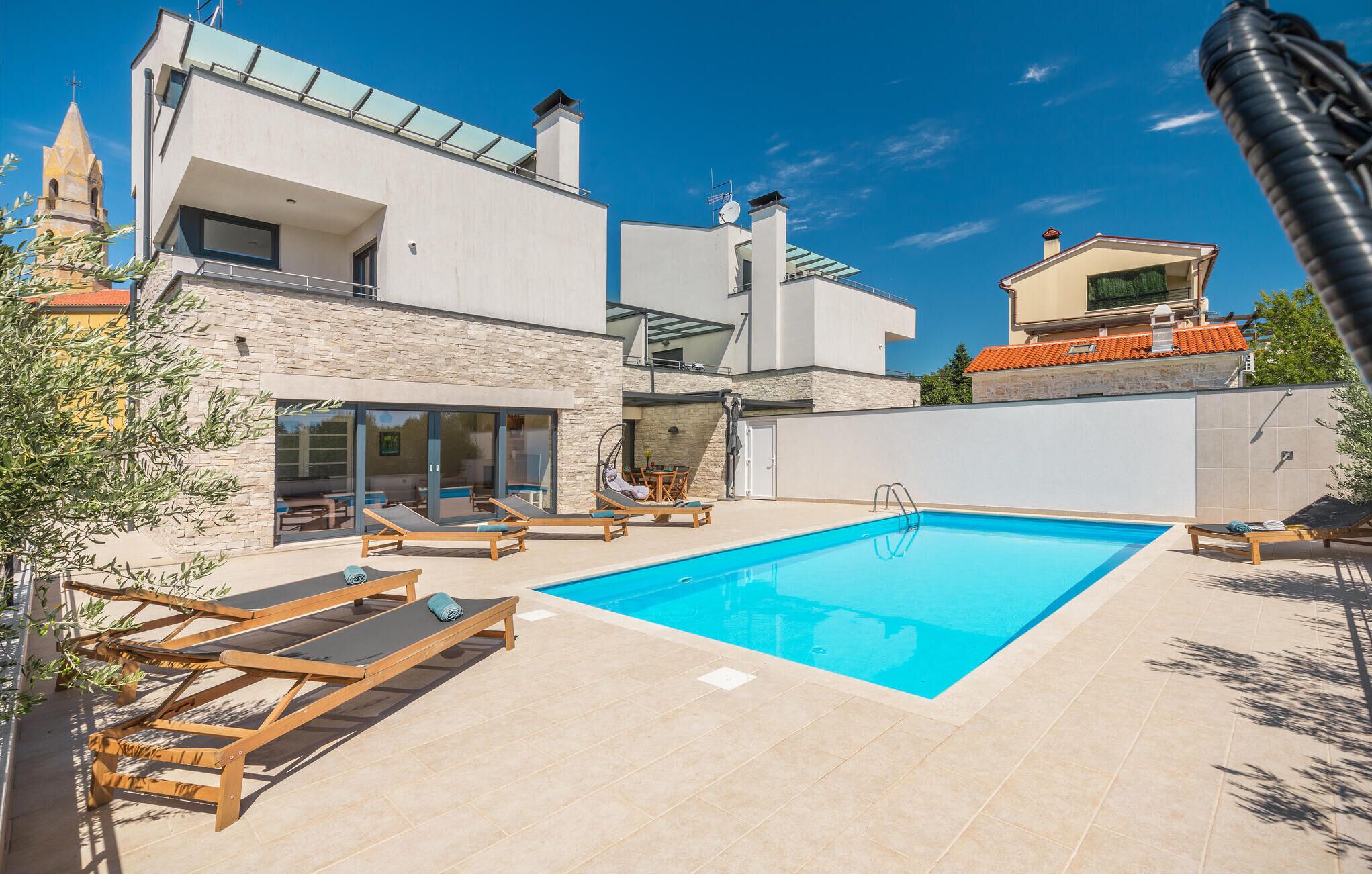 Una villa moderna con piscina, mobiliario exterior y fachada de piedra.
