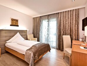 A hotel room with a bed, a desk, a chair, and a window with curtains.