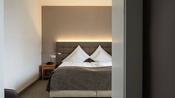 Quarto com cama, mesa de cabeceira, abajur e luminária na parede.