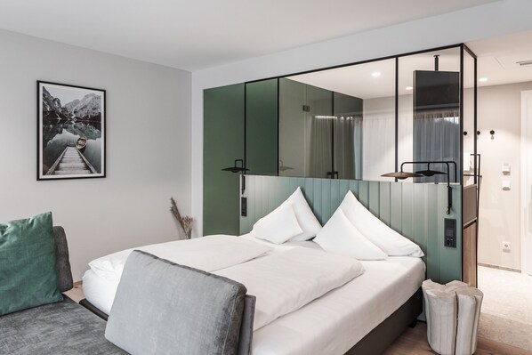 A modern hotel room with a large bed, a seating area with a sofa and armchair, a large mirror, and a framed picture on the wall.