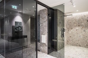 A modern bathroom with a glass shower enclosure, marble walls, and a visible hand dryer.