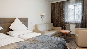 Ett hotellrum med en säng, en soffa, ett litet bord och ett fönster med gardiner.
