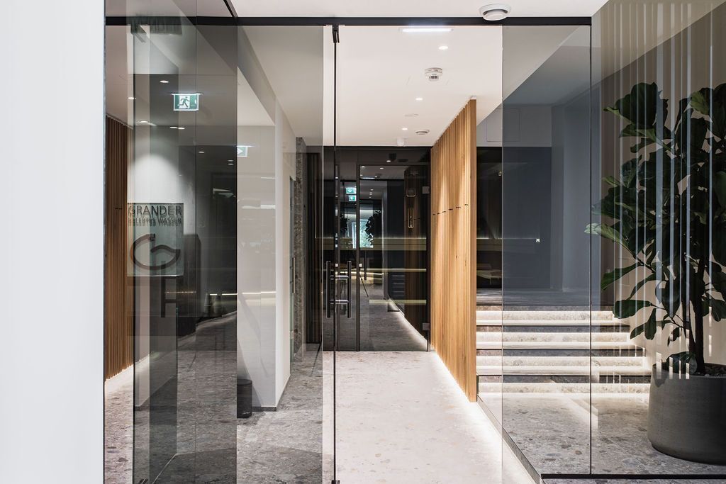 A modern hotel lobby with a glass door entrance, a wooden staircase, and a potted plant.