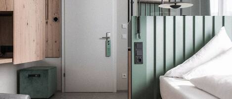 A room with a bed, a green cabinet, a small green ottoman, and a door.