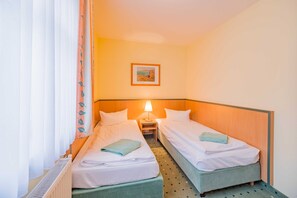 Una camera d'albergo con due letti singoli, un comodino con una lampada, un termosifone e un quadro appeso al muro.