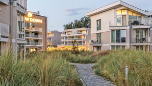 A modern hotel with a paved pathway, multiple balconies, and a visible restaurant area.