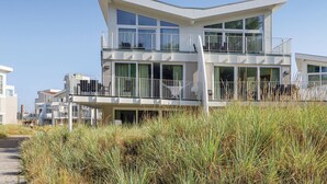 A modern two-story beachfront building with balconies, large windows, and a flat roof.