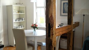 Ein Essbereich mit einem runden Tisch, weißen Stühlen, einer Vase mit Blumen, einem weißen Schrank mit Geschirr und einer Holzbalkenstruktur.