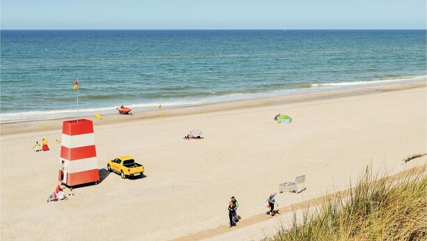 A beach with a lifeguard tower, a yellow vehicle, and people relaxing. - Beach front home in Ringkøbing with sauna (Ringkøbing)