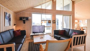 A cozy cabin interior with a wooden ceiling, a large window, a TV, and a dining area. - Beach front home in Ringkøbing with sauna (Ringkøbing)