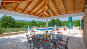 Un espacio al aire libre cubierto con piscina, mesa de comedor y sillas, con vistas a un paisaje montañoso.