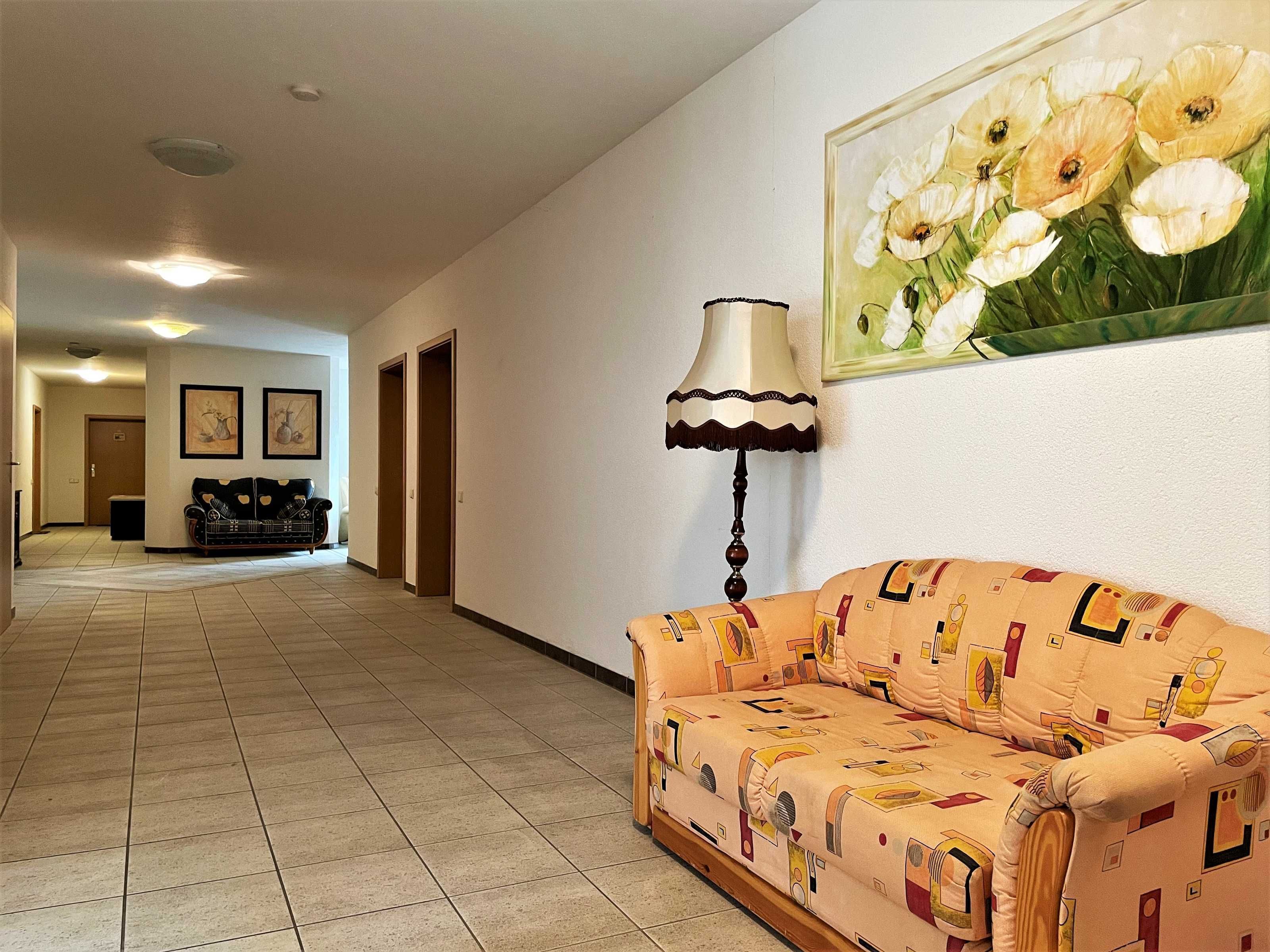 A hallway with a sofa and a lamp, a painting of flowers, and a door at the end.