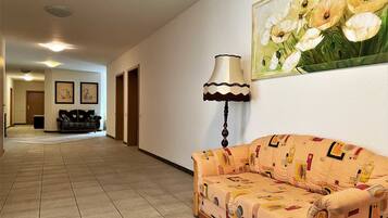 A hallway with a sofa and a lamp, a painting of flowers, and a door at the end.