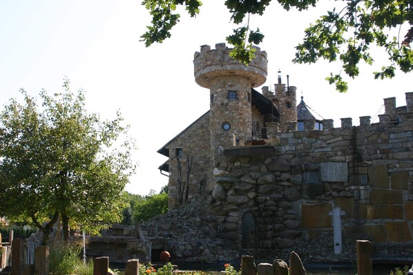 A stone castle with a round tower, surrounded by trees and stone walls.