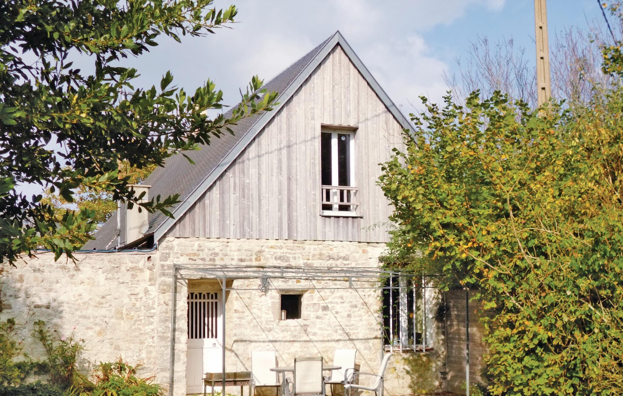 A rustic stone building with a gabled roof, a small balcony, and a stone wall entrance.