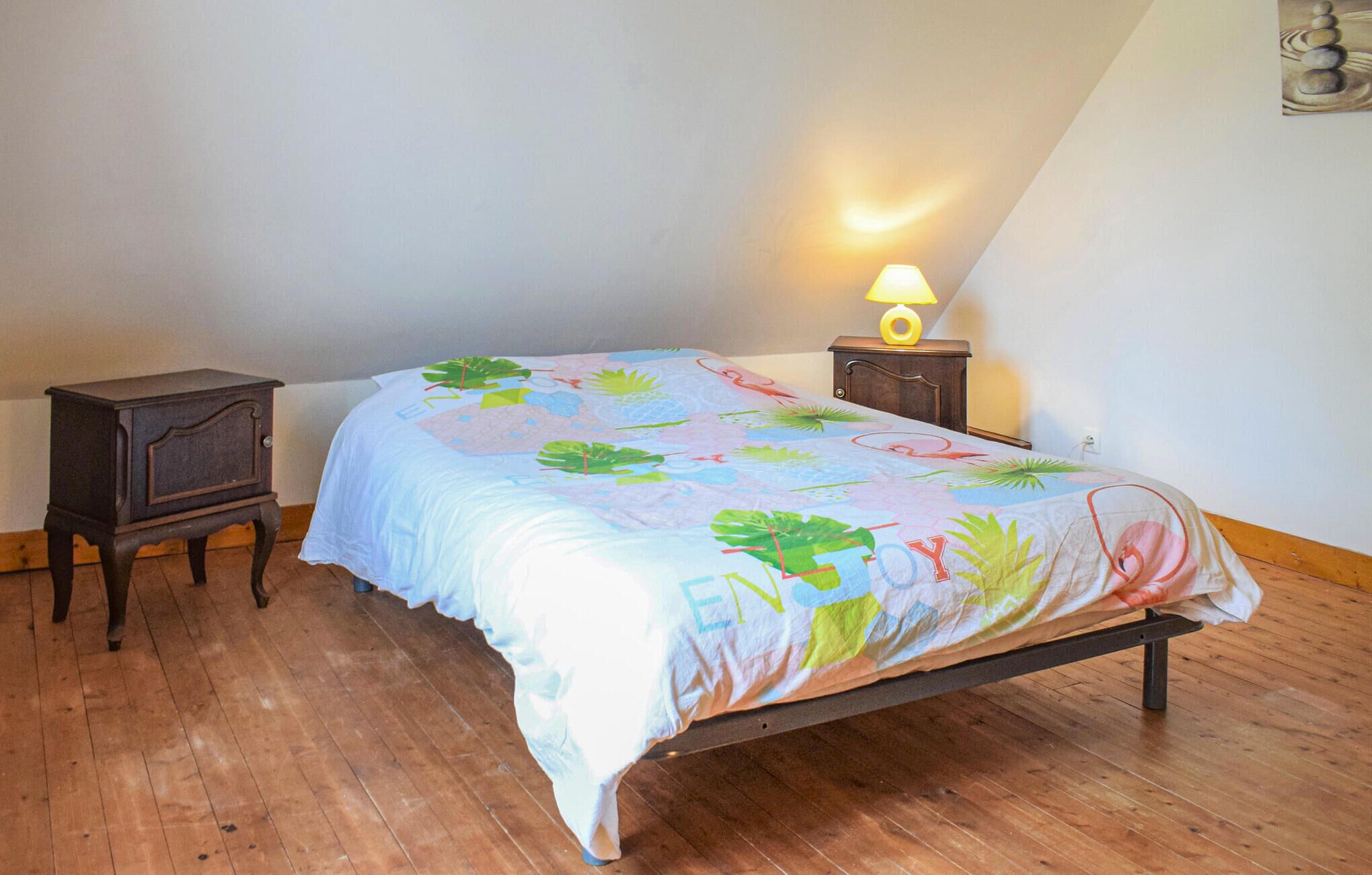 Un dormitorio con una cama, una mesita de noche, una lámpara y suelo de madera.