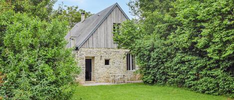 A rustic stone building with a wooden roof, surrounded by lush greenery.