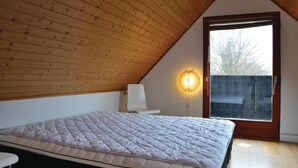 A bedroom with a sloped ceiling, a bed, a chair, a wall-mounted light, and a window with a view of trees. - 4 bedroom lovely home in Græsted (Græsted)