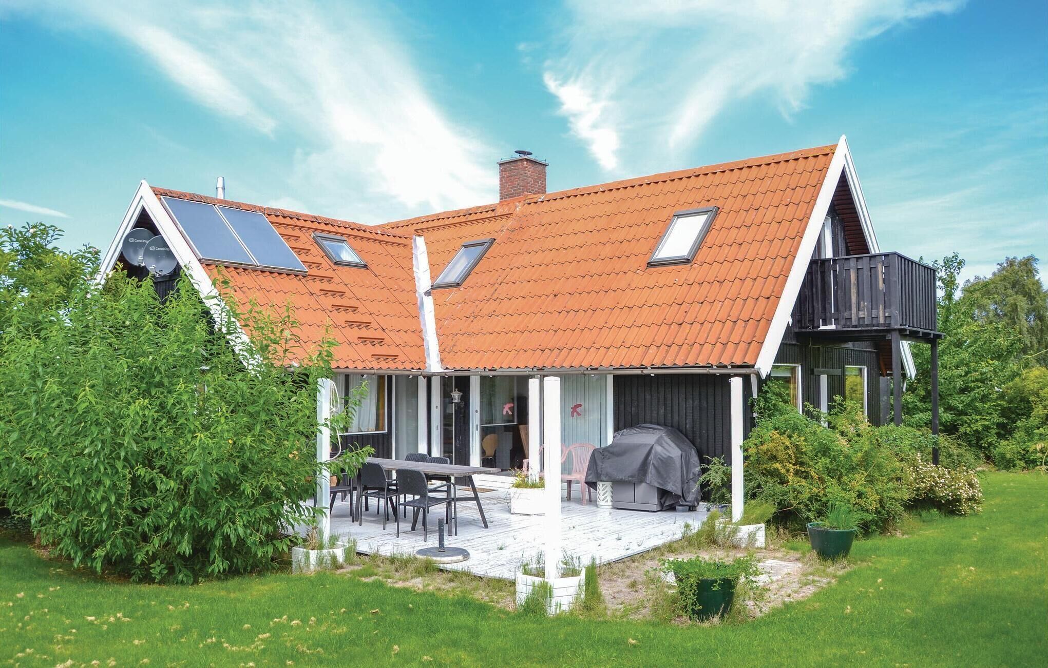Une maison moderne dotée d’un toit en pente, de panneaux solaires et d’un patio couvert aménagé avec du mobilier d’extérieur.