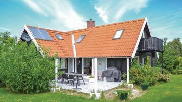 Une maison moderne dotée d’un toit en pente, de panneaux solaires et d’un patio couvert aménagé avec du mobilier d’extérieur.