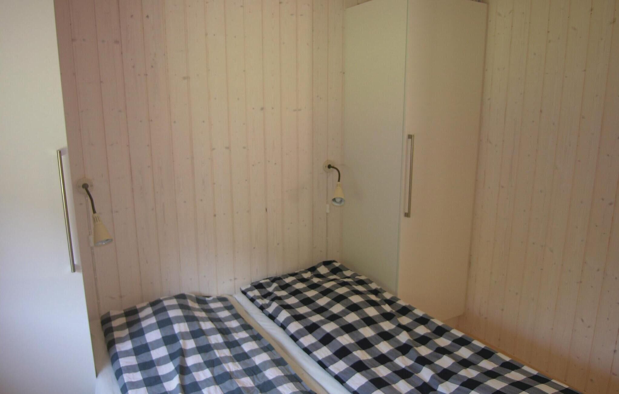 Een kleine kamer met een enkel bed, een garderobe en een lamp aan de muur.