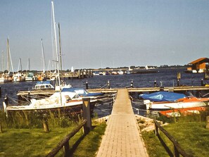 A marina with boats docked, a wooden walkway leading to the water, and a distant pier. - Holiday Bungalow - Bungalow (Reinberg)