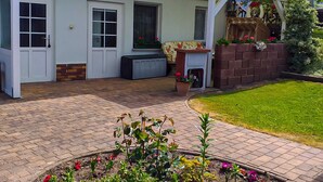 A house with a covered patio, a brick fireplace, and a garden with colorful flowers. - Holiday Bungalow - Bungalow (Reinberg)
