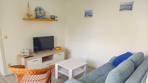 A living room with a sofa, a television, a small table, and a wicker chair. - Holiday Bungalow - Bungalow (Reinberg)