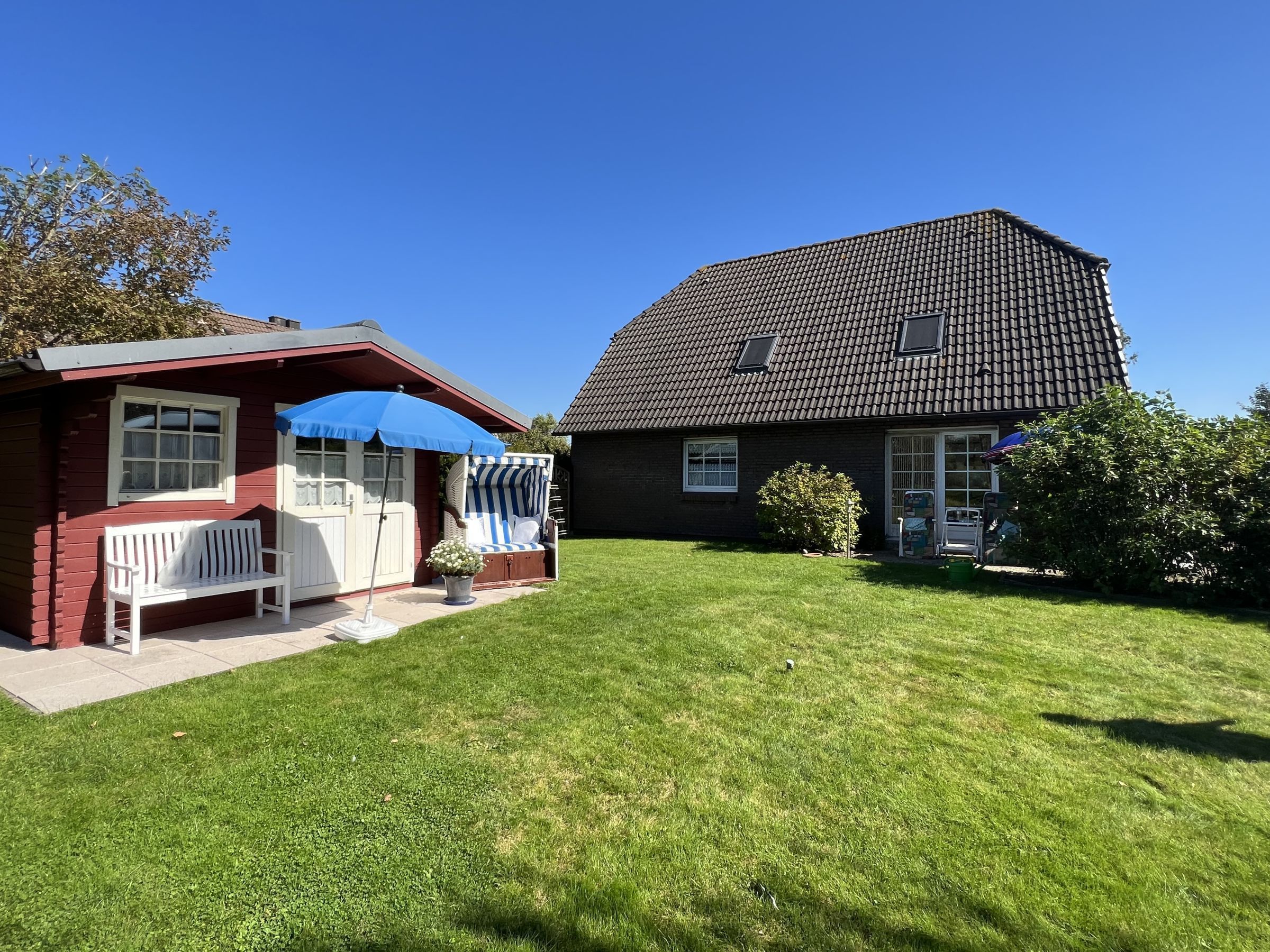 A two-story house with a red exterior, a blue umbrella, and a white bench.