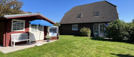 Une maison à deux étages avec une façade rouge, un parasol bleu et un banc blanc.