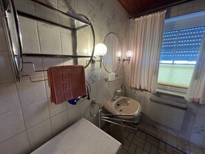 A bathroom with a sink, mirror, towel rack, and a window with curtains.