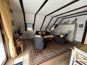 A cozy loft-style room with a high ceiling, a sofa, a chair, a small table, and a cabinet.