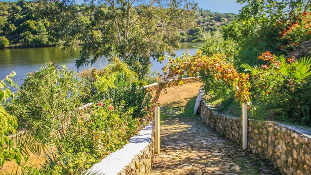 Un sendero de piedra que lleva a un arco de madera rodeado de vegetación exuberante y un lago.