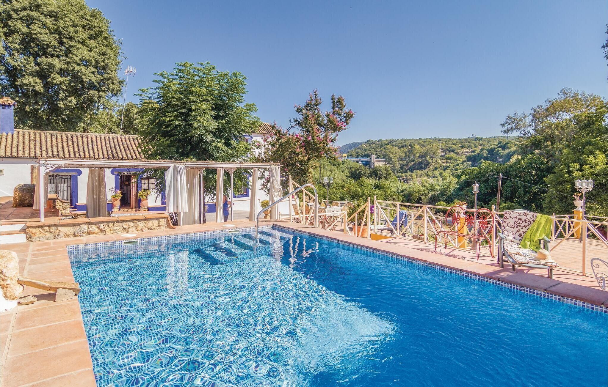 Piscina com borda em azulejo, rodeada por espreguiçadeiras e uma área coberta com vista para as colinas.